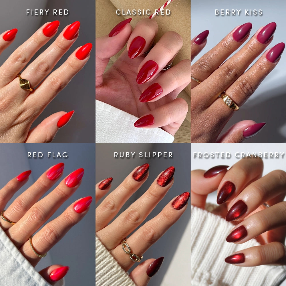 Six hands display different shades of red press-on nails from the glamnetic "Seeing Red" set—fiery red, classic red, berry kiss, red flag, ruby slipper, and frosted cranberry—each labeled on short almond-shaped nails. Some fingers are adorned with rings, and the vibrant look is easily achieved with these glamnetic press-on nails for a flawless finish. - Product image