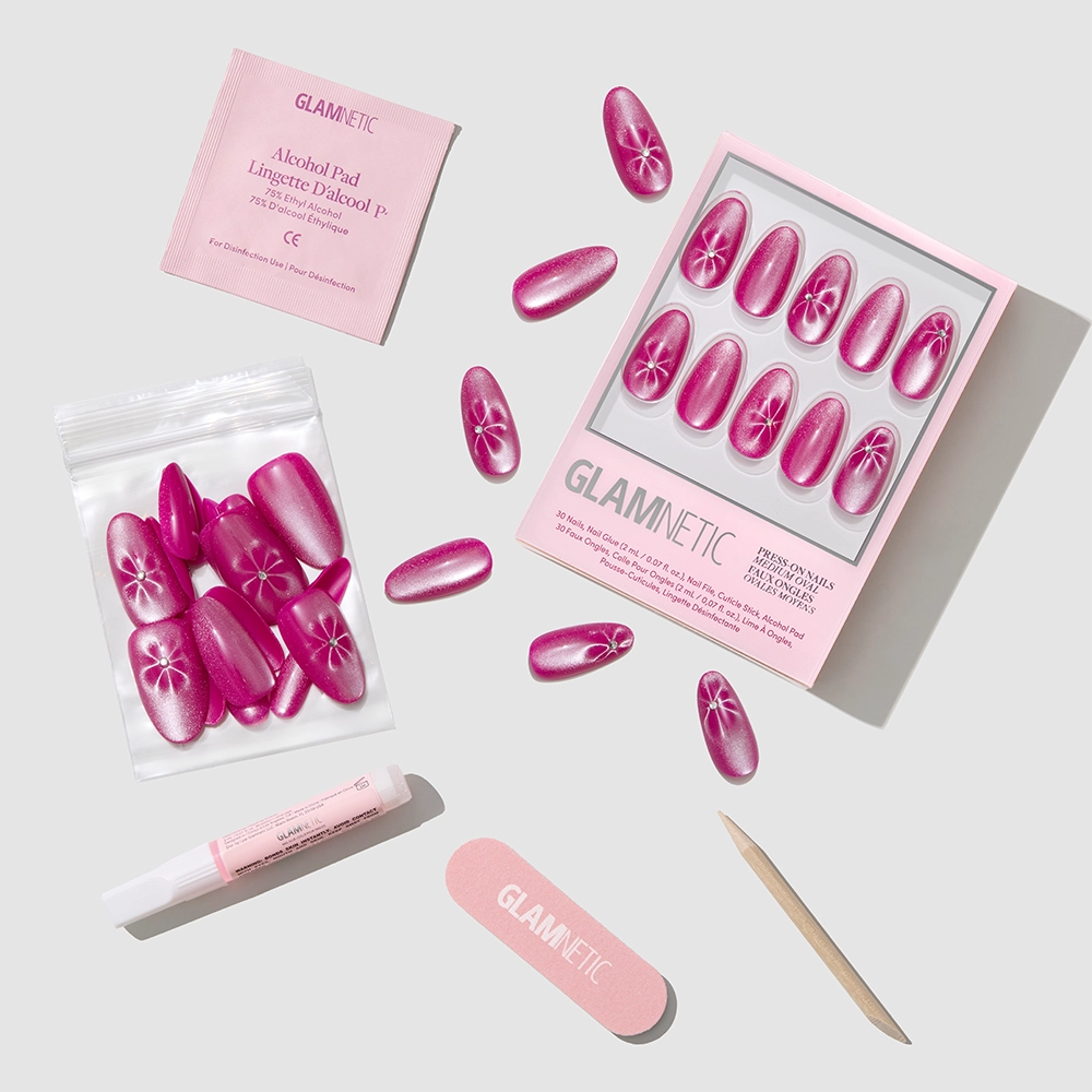 The Rosy Siren by glamnetic features bright pink magenta rose nails with white floral designs, plus a nail file, wooden stick, glue, alcohol pad, and extra nails—all neatly arranged on a light gray background. - Product image
