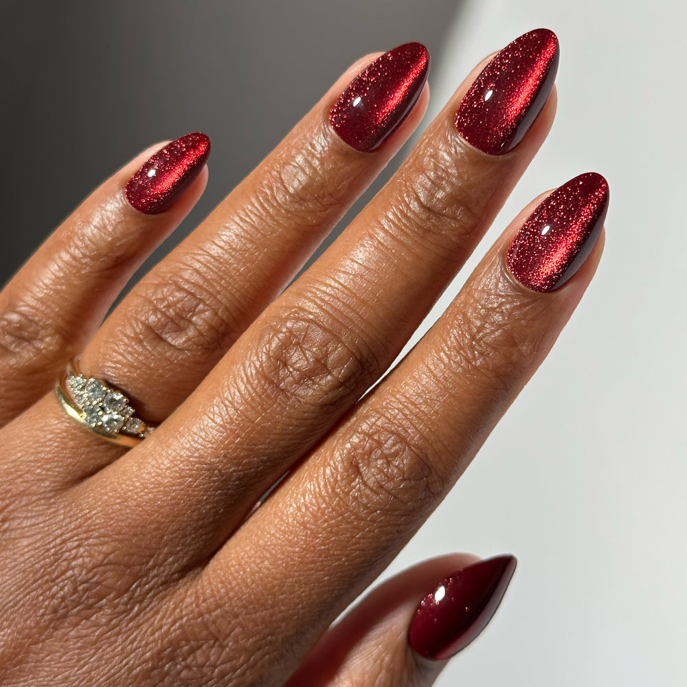 A hand with short almond nails painted in Ruby Slipper, a shimmering, deep red metallic polish from glamnetic.