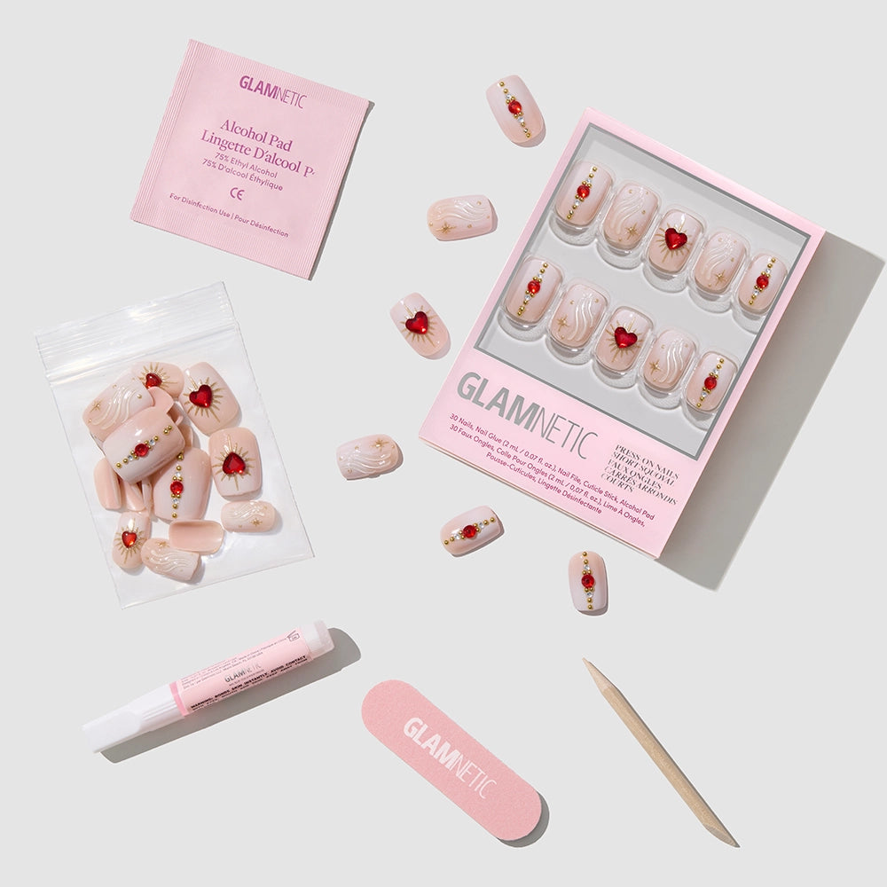 A flat lay of glamnetic Ruby press-on nails featuring pink and red floral glossy nail art, with nail glue, alcohol pad, nail file, wooden cuticle stick, and extra short squoval nails on a white background. - Product image