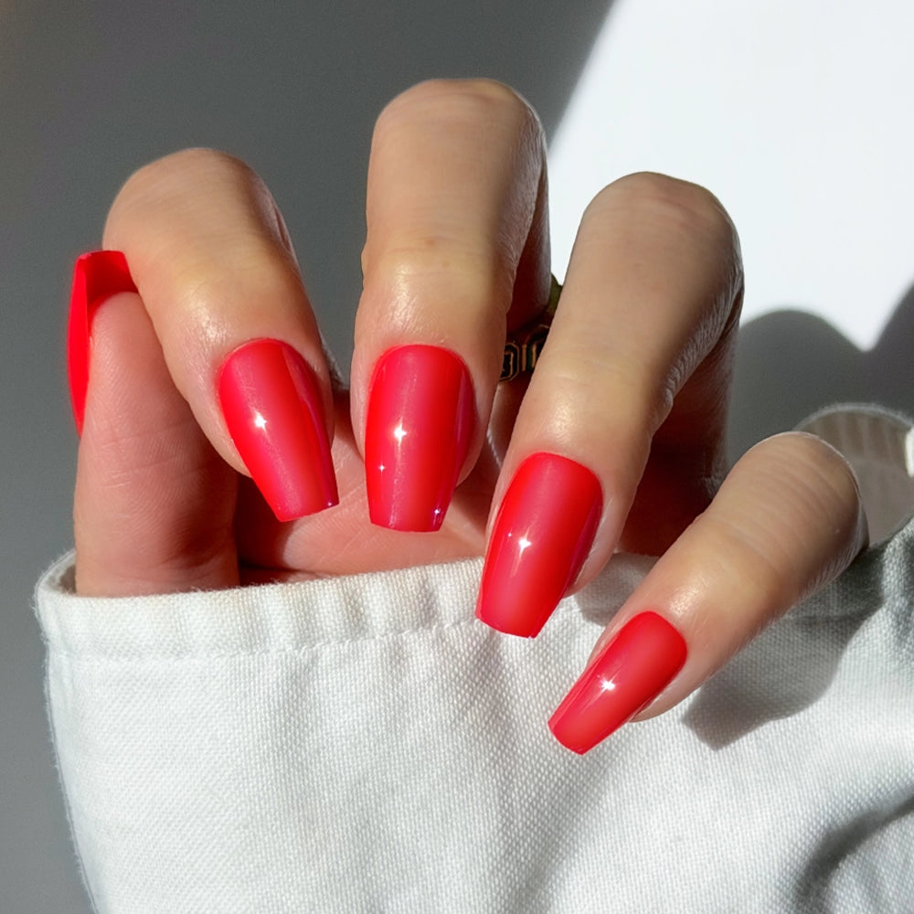 A hand with long, glossy red coffin nails in glamnetic's Runway Red set is shown against a white background. The shiny, salon-quality manicure and crisp white sleeve create a chic, polished look.