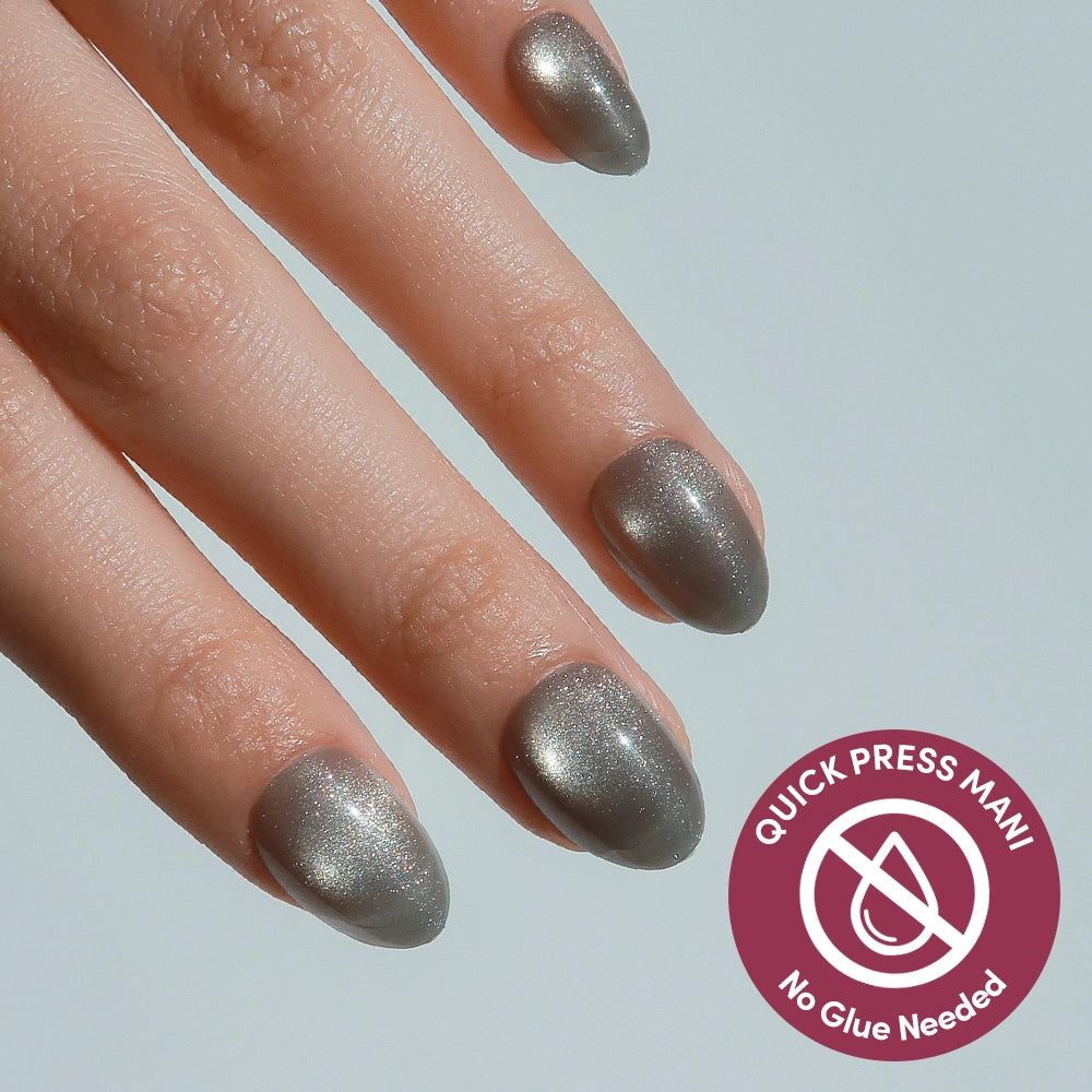 A close-up of a hand with short, oval-shaped glamnetic Sparkly Moss press-on nails in metallic silver. A corner badge reads "QUICK PRESS MANI No Glue Needed" with an icon showing a crossed-out nail and glue.