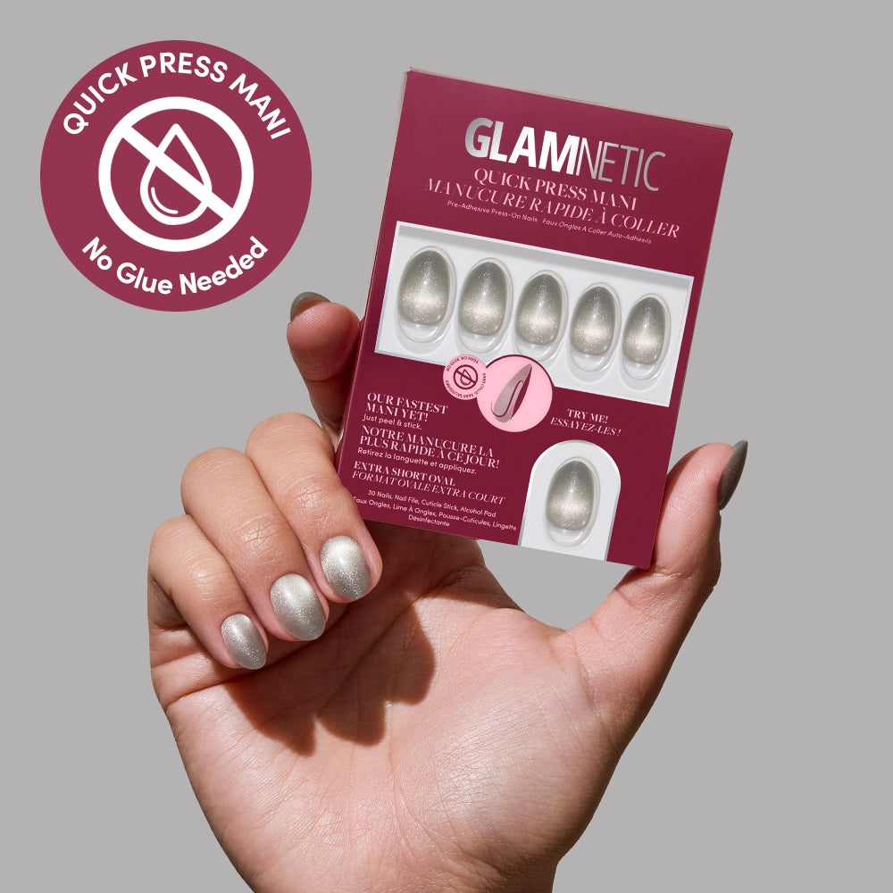 A hand with metallic silver press-on nails holds a glamnetic Sparkly Moss kit box. The box highlights quick stick-on, no-glue silver nails, with a “No Glue Needed” badge in the top left corner.