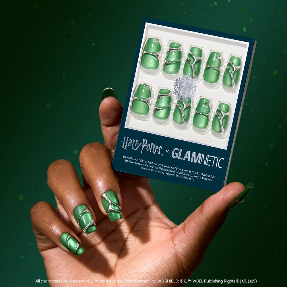 A hand with shiny green velvet coffin nails holds a glamnetic Salazar Slytherin™ box containing matching press-on nails, set against a green background.