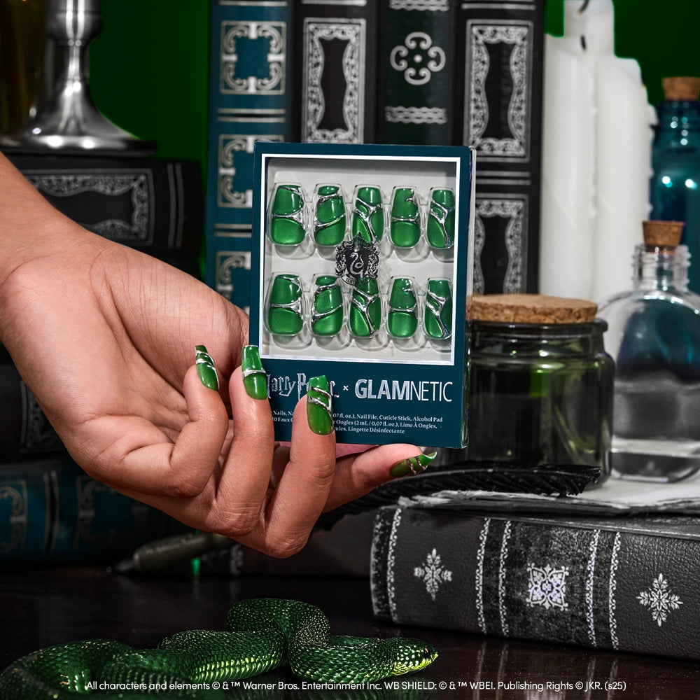 A hand with green velvet coffin-shaped nails holds a box of the Salazar Slytherin™ nail set by glamnetic; Harry Potter books and potion bottles appear in the background. - Product image