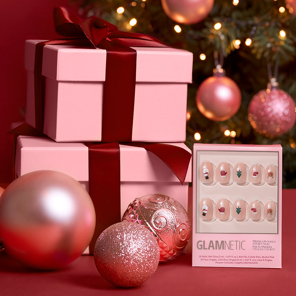 Santa's Babies - A box of Santa’s Babies festive holiday press-on nails in a short oval shape, placed next to two pink gift boxes and decorative ornaments.