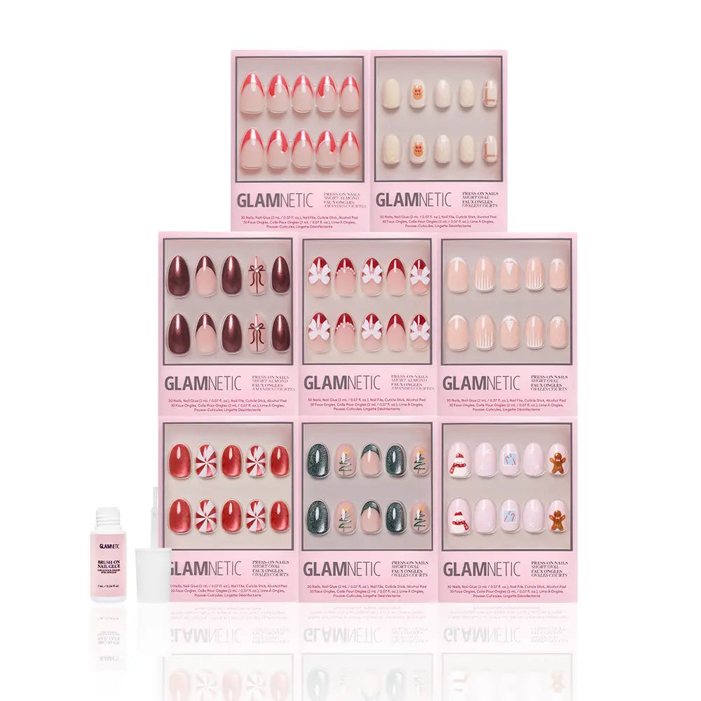 Eight boxes of glamnetic Santa's Workshop press-on nails are stacked together, with a small bottle of nail glue in front. The festive holiday designs feature candy canes, snowflakes, and gingerbread men. - Product image