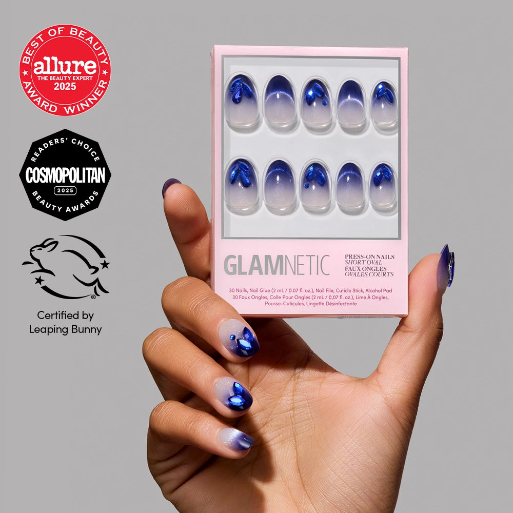 A hand with blue and white gradient glamnetic Sapphire Press-On Nails holds a glamnetic box. Allure, Cosmopolitan, and Leaping Bunny certification logos are displayed on the left.