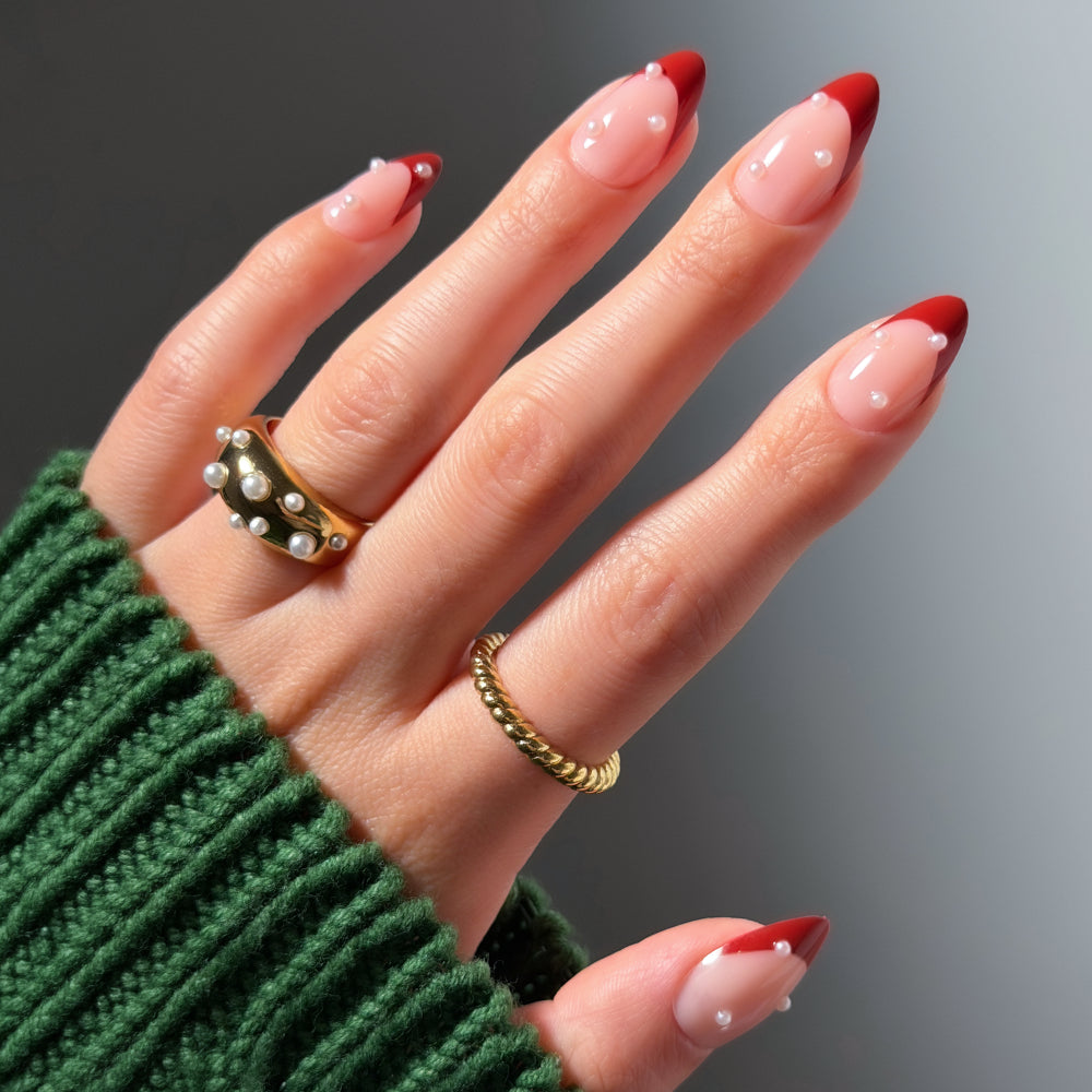 Glamnetic Scarlet Pearl short almond press-on nails featuring red French tips, accented with small white pearls on the nail bed.