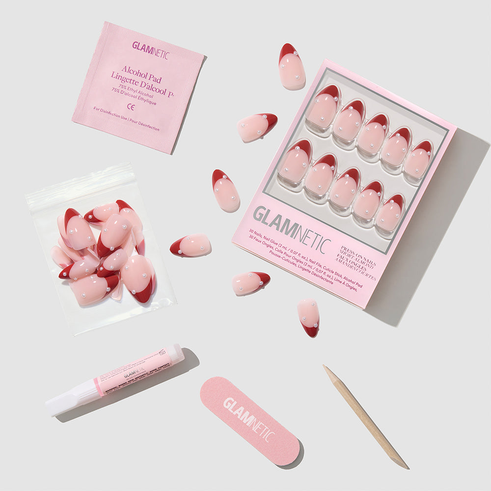 Glamnetic Scarlet Pearl short almond press-on nails featuring a red French tip design with a pearl accent, including adhesive, an alcohol pad, a nail file, and a cuticle pusher. - Product image
