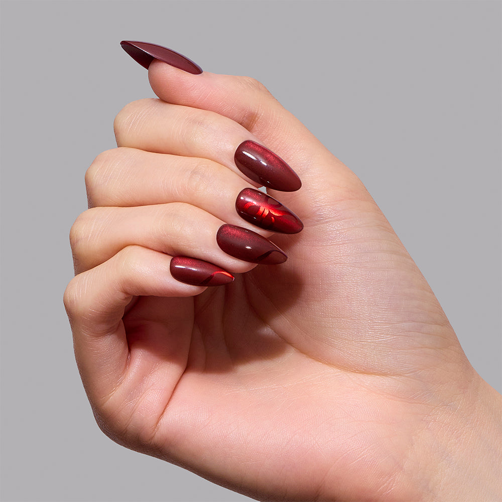 Short almond nails in a deep red magnetic velvet effect featuring a ribbon-like accent on the ring finger, showcasing the Scarlet Ribbons set by Glamnetic. - Product image