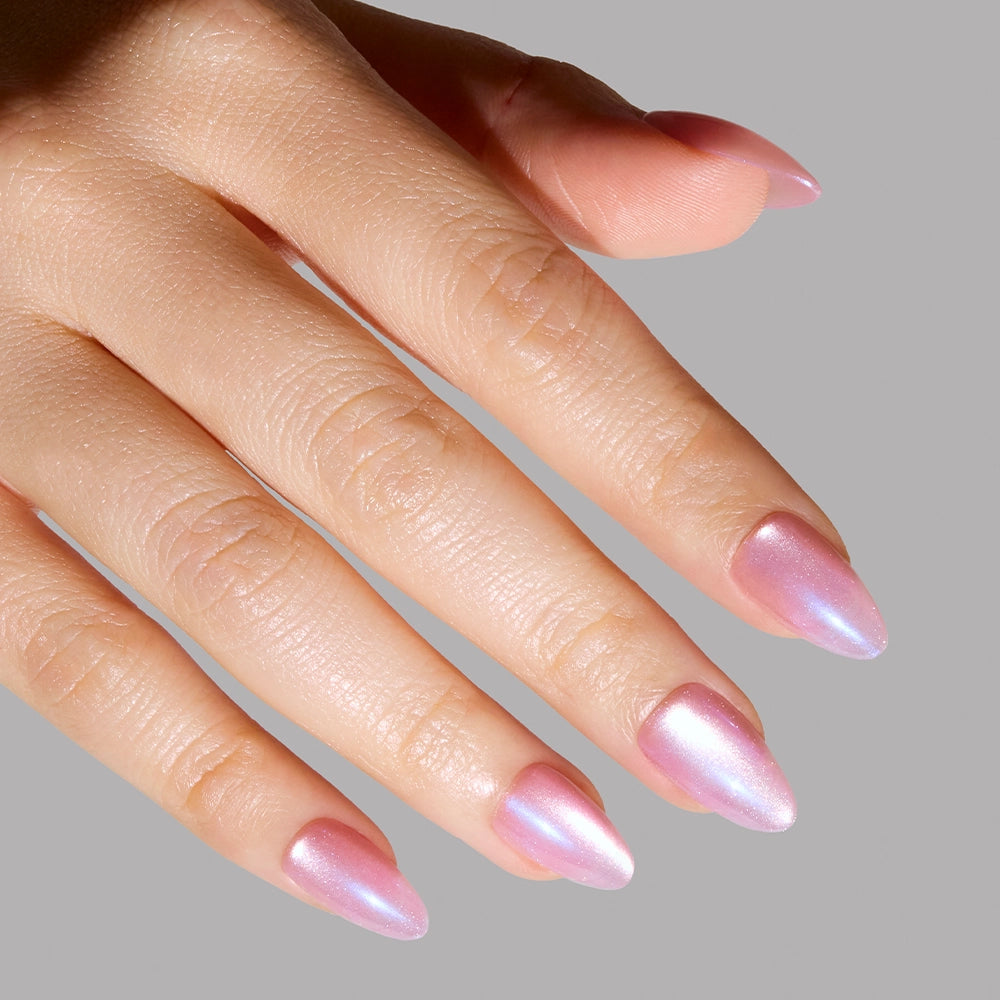 A hand with short almond nails is painted in glamnetics Seaspell, an iridescent pink polish with a shimmering velvet finish, shown against a plain gray background. - Product image
