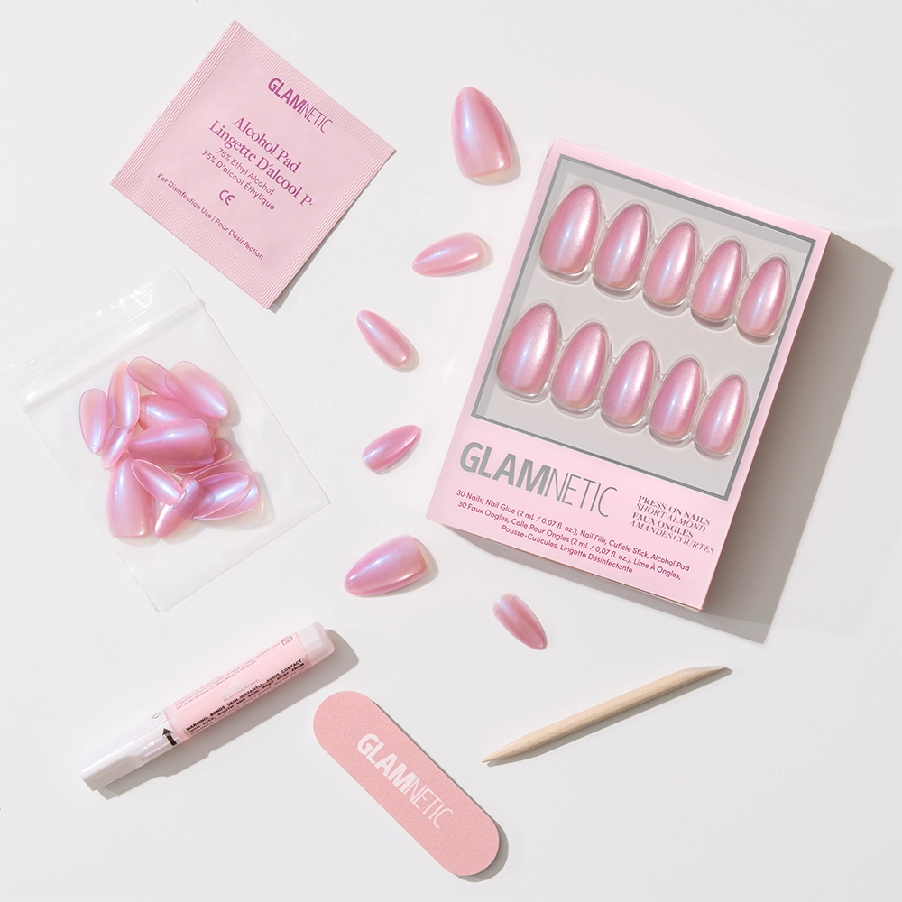 The glamnetic Seaspell set includes pink iridescent, short almond press-on nails with a velvet shimmer, plus nail glue, a wooden cuticle stick, file, extra nails, and an alcohol pad—all displayed on a white background. - Product image