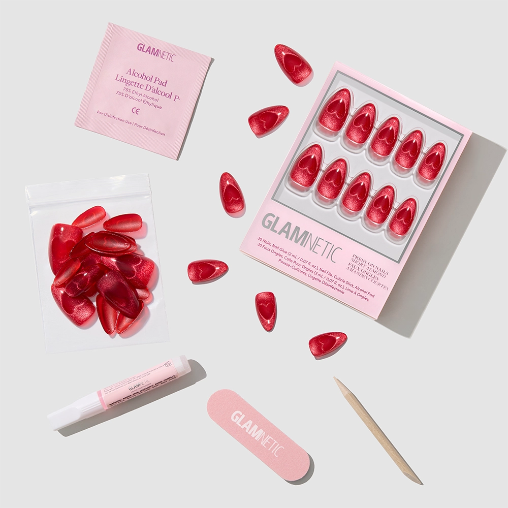 The glamnetic "Sent with Love" set features short red velvet almond press-on nails with extra nails, nail glue, alcohol pad, nail file, and a wooden cuticle stick—beautifully arranged on a white background. - Product image