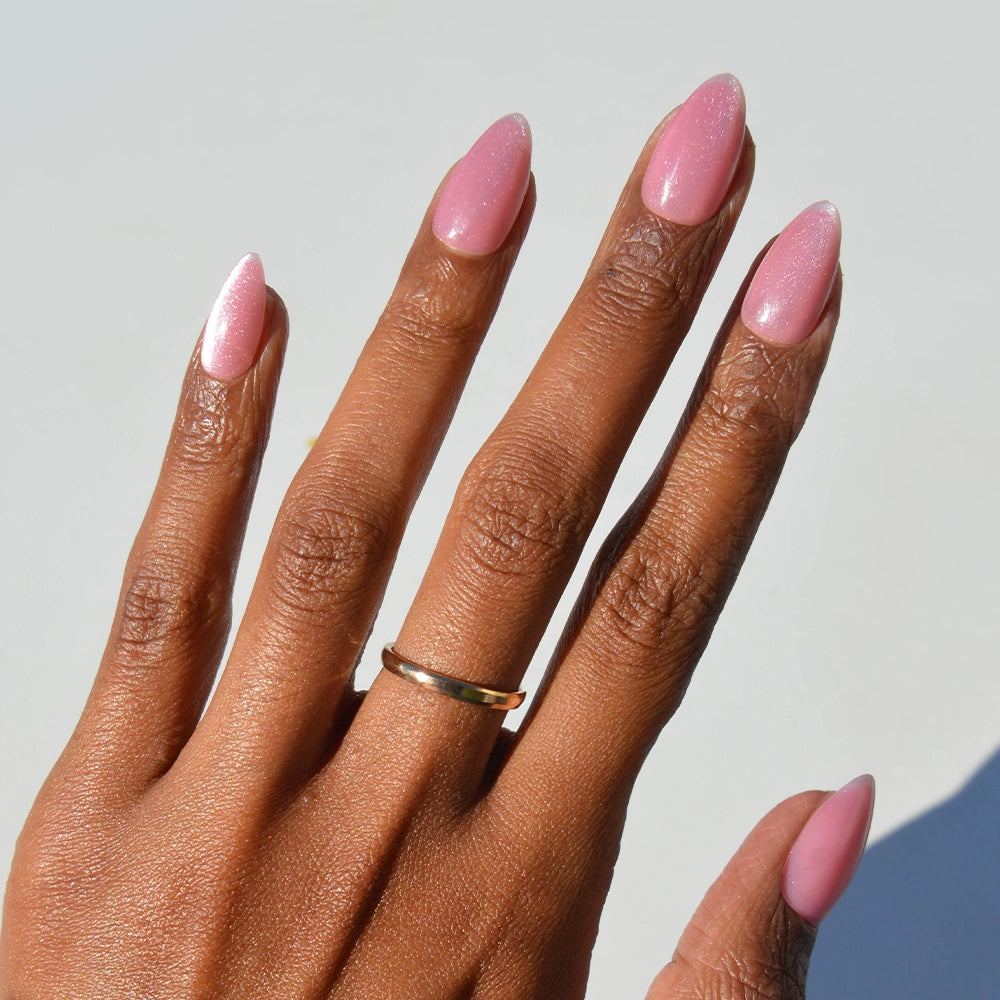 A hand with medium brown skin wears a simple gold ring and displays long nails painted in glossy rosy pink velvet—perfectly showcasing glamnetic’s Shine for You nail set against a light background. - Product image
