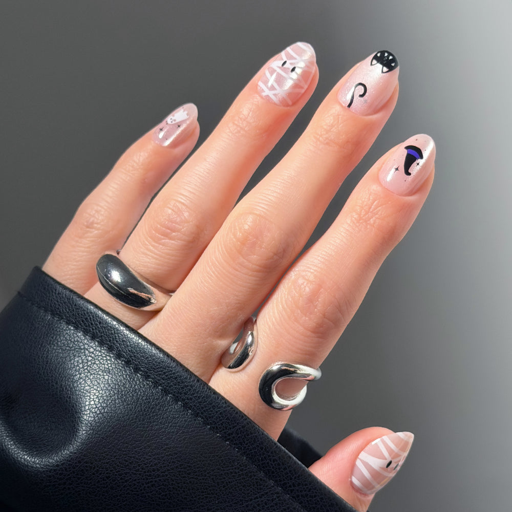 A hand with silver rings displays a short oval mani featuring the glamnetic Shriek Boutique press-on nails, showcasing minimalist abstract designs in black, white, and purple on a nude base. The person wears a black leather sleeve. - Product image