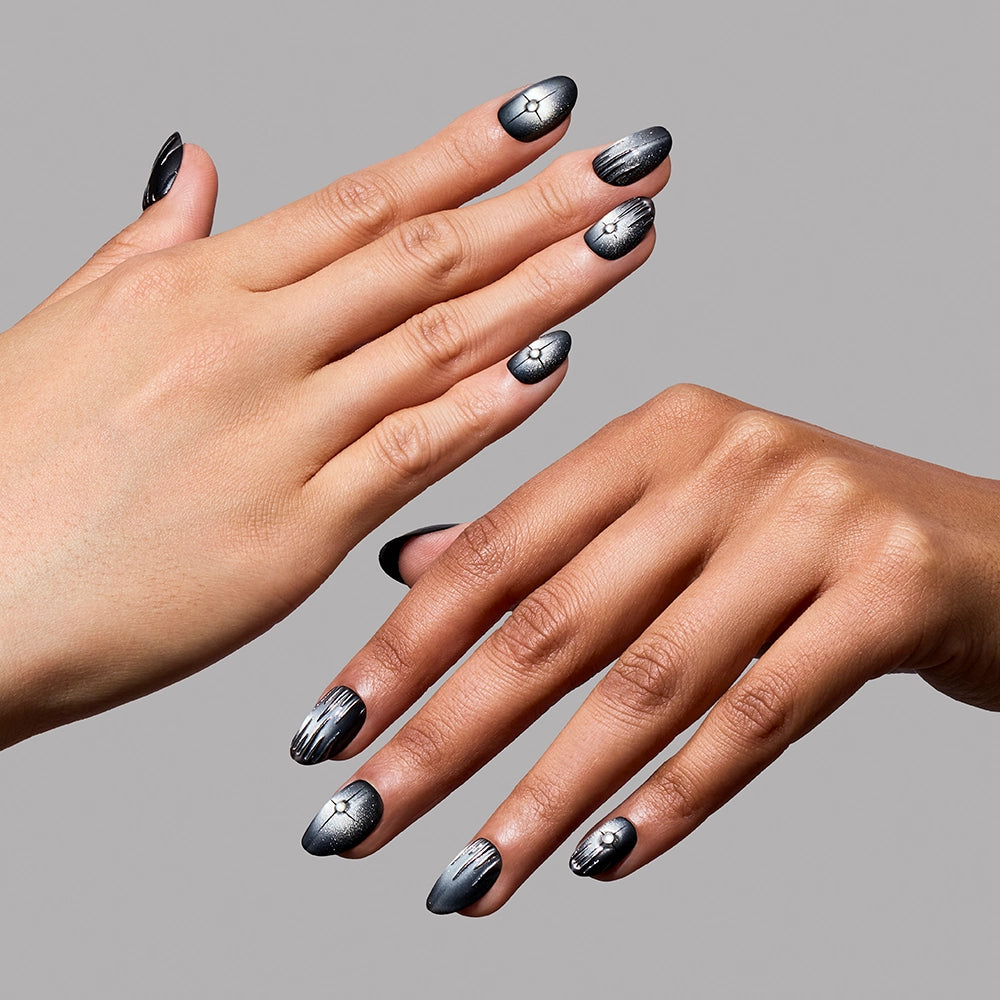 Two hands showcase black and silver metallic nail art, inspired by the Silver Daggers set from glamnetic, with abstract lines and crackled designs, against a plain gray background. - Product image