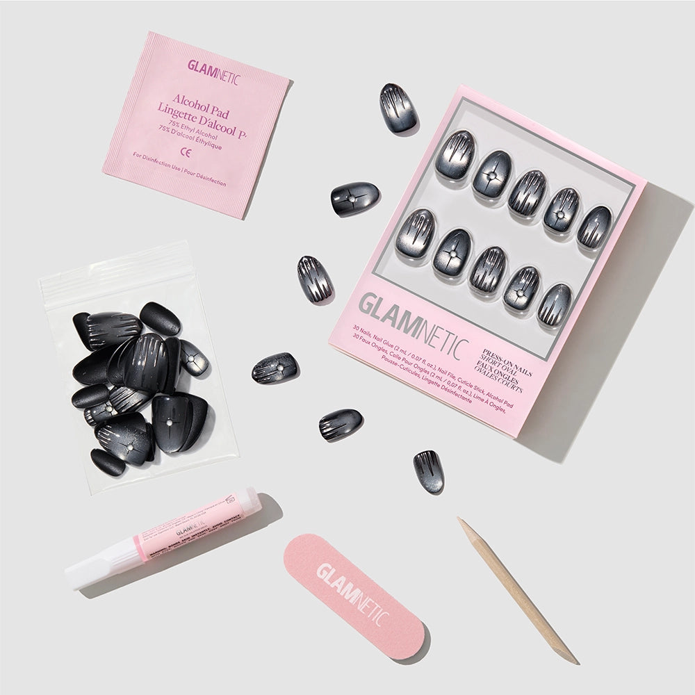 A set of black velvet press-on nails, along with glue, an alcohol pad, a nail file, a cuticle stick, and extra nails from glamnetic’s Silver Daggers collection are arranged neatly on a light gray background. - Product image