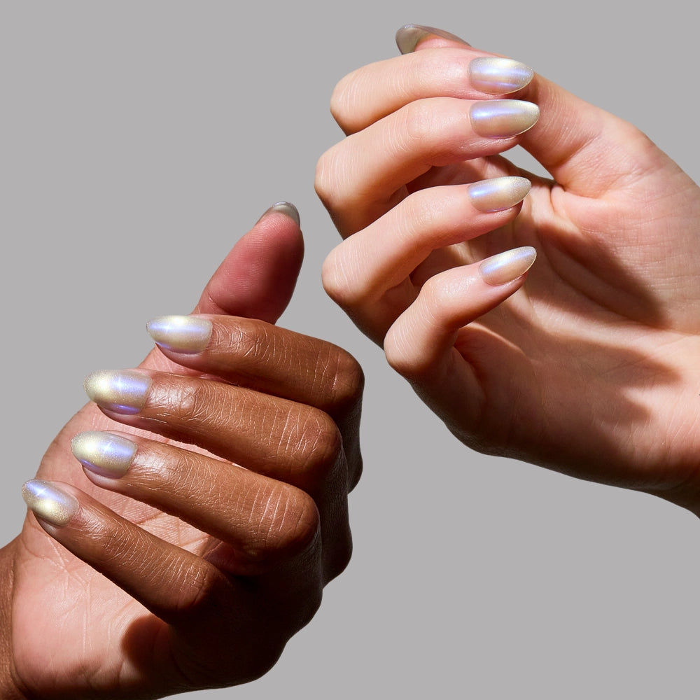 Two hands with different skin tones show off glamnetic's Silver Siren short oval nails, painted in iridescent, pearly polish against a plain gray background, capturing the essence of semi-sheer grey nails. - Product image