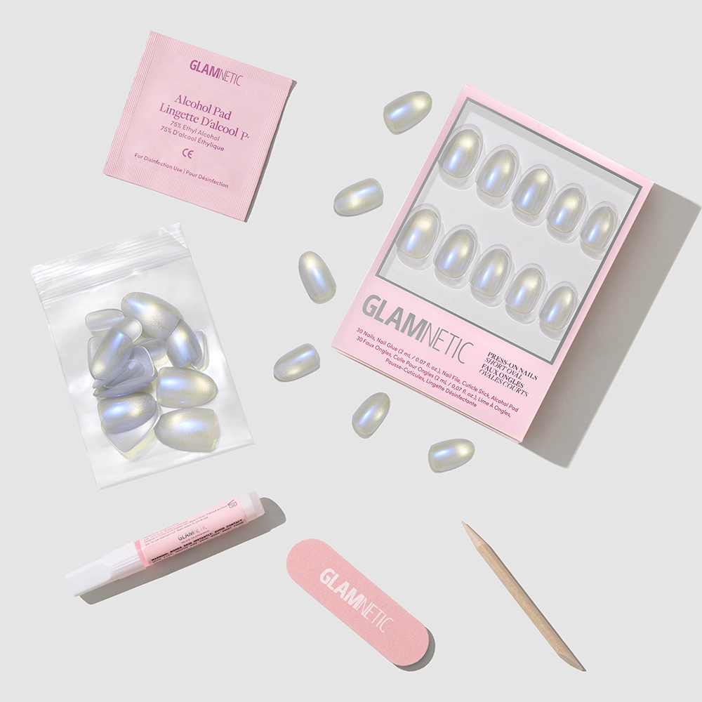 Flat lay of glamnetic Silver Siren press-on nails kit, showcasing iridescent blue chrome and semi-sheer grey short oval nails, with a pink nail file, cuticle stick, nail glue, cleansing pad, and extra nails on a light gray background. - Product image