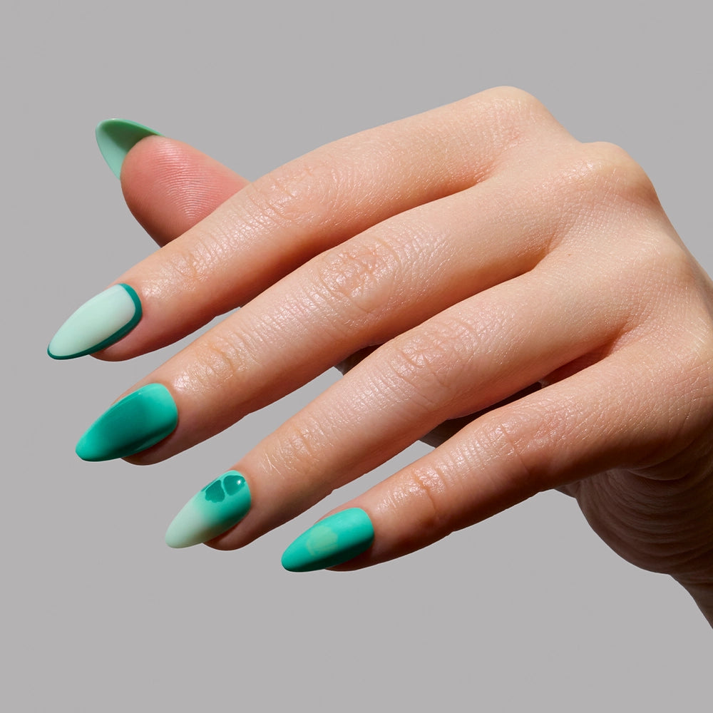 A hand with almond-shaped glamnetic Siren Green Press-On Nails, in shades of green and mint with minimalist art and a glossy finish, displays mermaid-inspired style against a plain gray background. - Product image