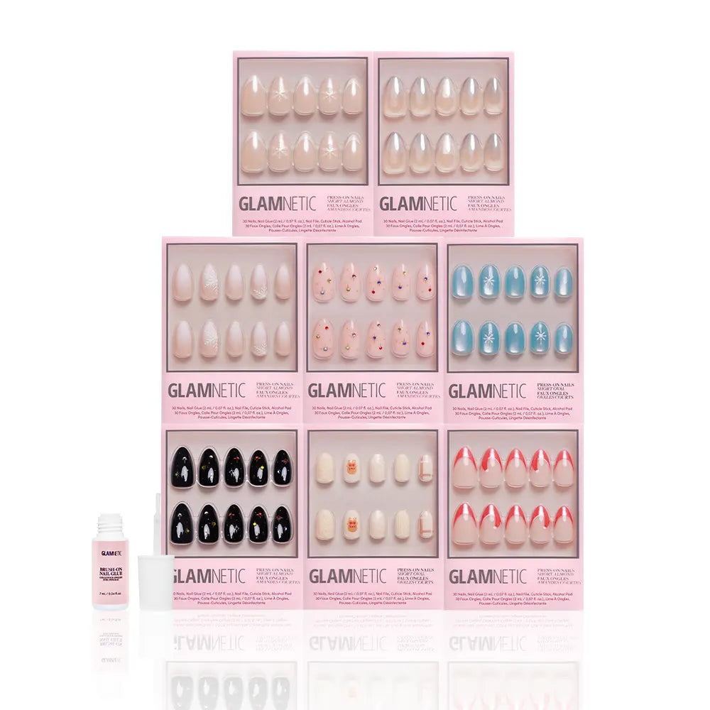 Eight boxes of glamnetic's Snow Place Like Home Collection festive press-on nails, featuring assorted colors and designs, are arranged in two rows with a small glamnetic-branded bottle on the left, all set against a white background. - Product image