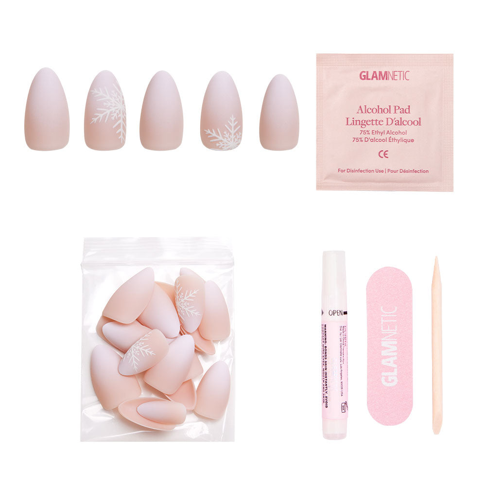 The glamnetic Snowdrift set includes pink, almond-shaped matte gradient press-on nails with white snowflake accents, plus an alcohol pad, pink nail file, cuticle stick, nail glue, and extra nails in a clear bag. - Product image