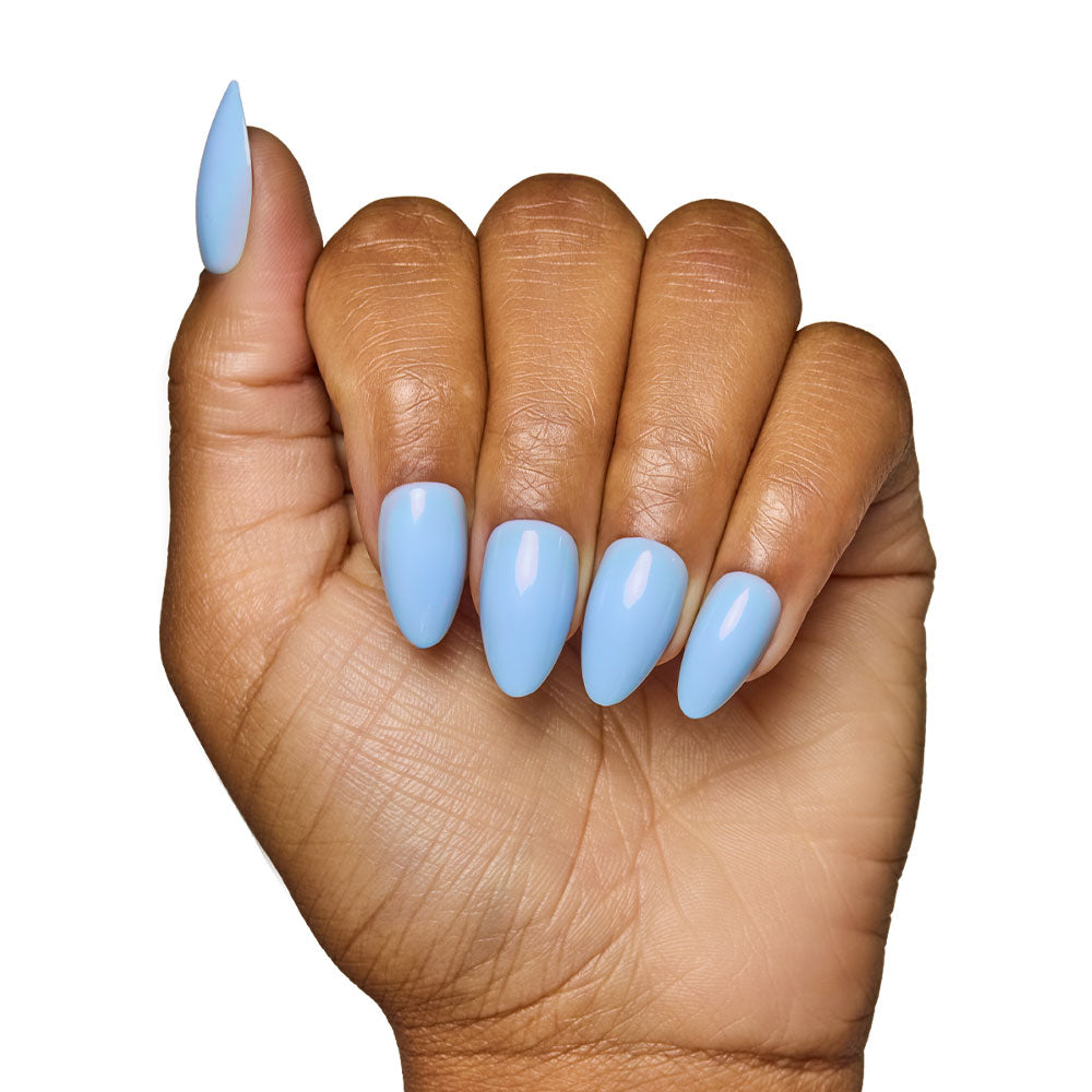 A hand with medium brown skin tone displays short almond nails painted with glamnetics Soft Blue Nail Set, featuring a glossy finish, elegantly set against a white background. - Product image