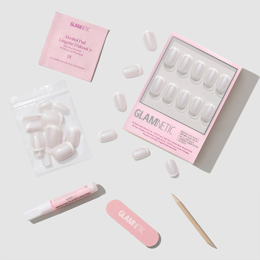 The Soft Tulle press-on nail set by glamnetic features short, squoval-shaped pink nails and comes complete with a nail file, cuticle stick, glue tube, alcohol pad, and extra nails—each item displayed elegantly on a light gray background. - Product image