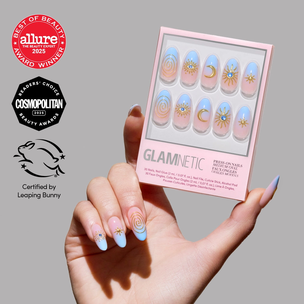 A hand with pastel pink and blue ombre French tip press-on nails featuring gold star and swirl designs holds the glamnetic Spirited Sky nail set, shown with Allure and Cosmopolitan Beauty Awards and Leaping Bunny cruelty-free certification.