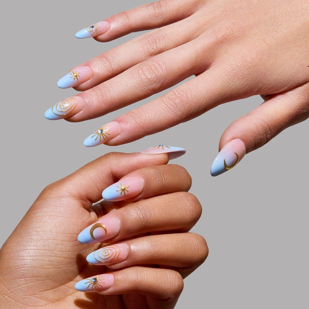 Four hands display glamnetic's Spirited Sky long, almond-shaped press-on nails in pastel blue and nude, featuring gold stars, moons, and spirals, set against a plain gray background. - Product image