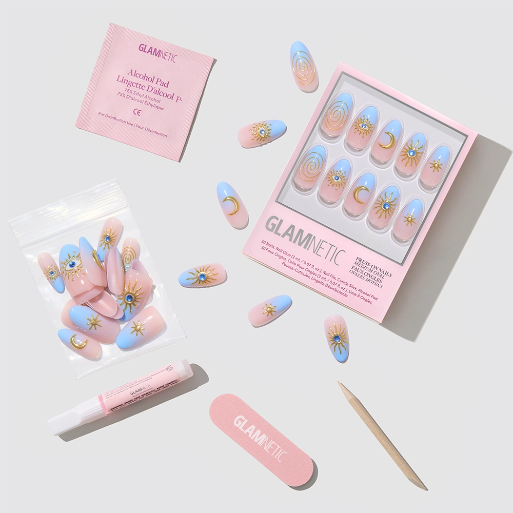 The glamnetic Spirited Sky set features cruelty-free press-on nails with pink and blue ombre French tips, gold sun and moon accents, plus nail glue, alcohol pad, cuticle stick, nail file, and extra nails—all arranged on a light background. - Product image