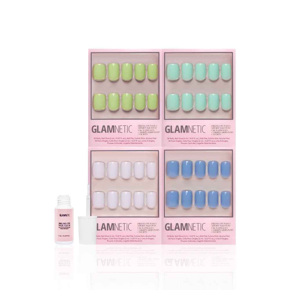 Four boxes of glamnetic Spring Showers short squoval press-on nails in pastel green, mint, lilac, and blue are arranged in a grid. A small open bottle of nail glue and an applicator sit in front, showing off their glossy finish. - Product image