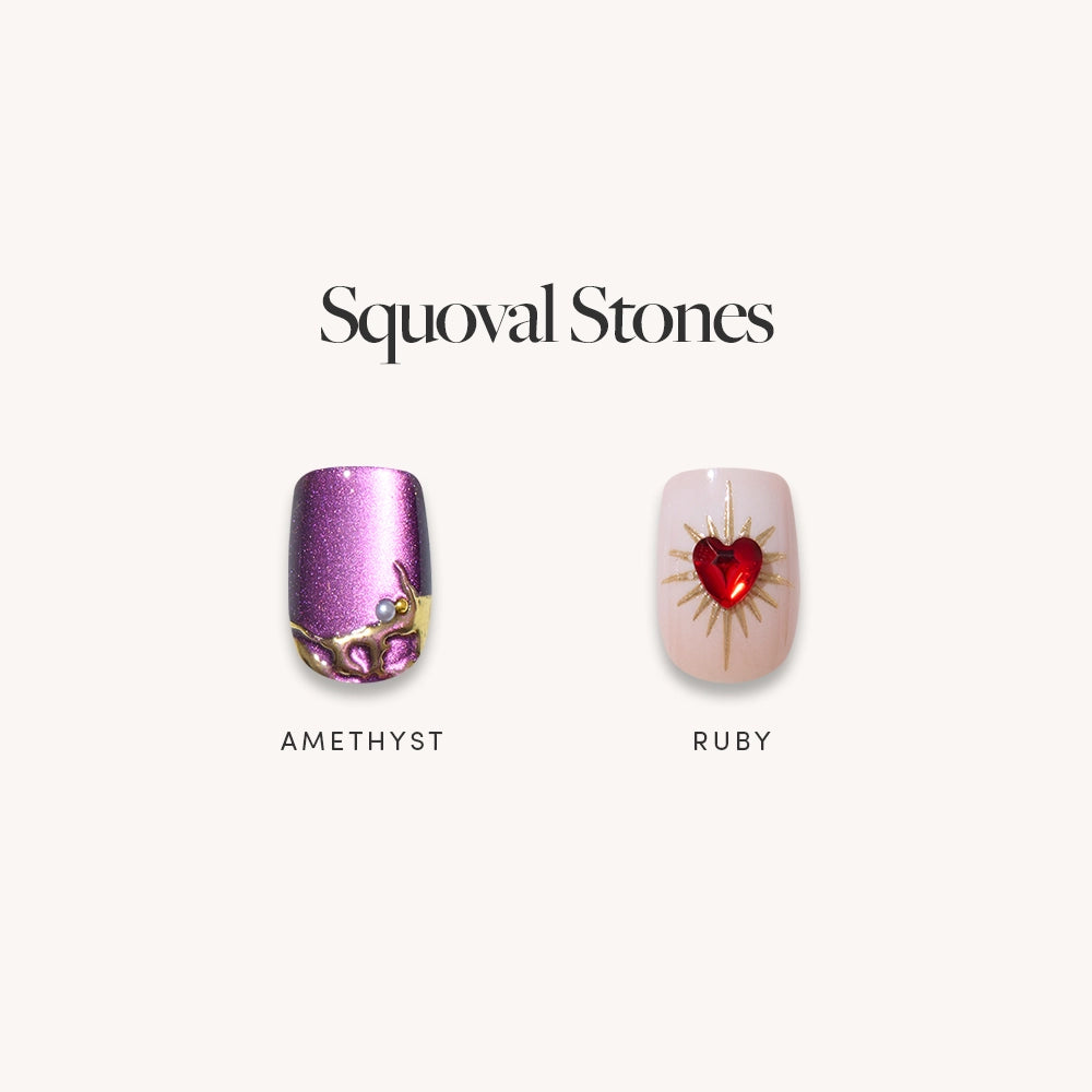 Two short squoval press-on nails from glamnetic’s Squoval Stones set are displayed: “AMETHYST” is a shimmery purple with gold and amethyst 3D art; “RUBY” is pale with a red gem and gold sunburst. - Product image