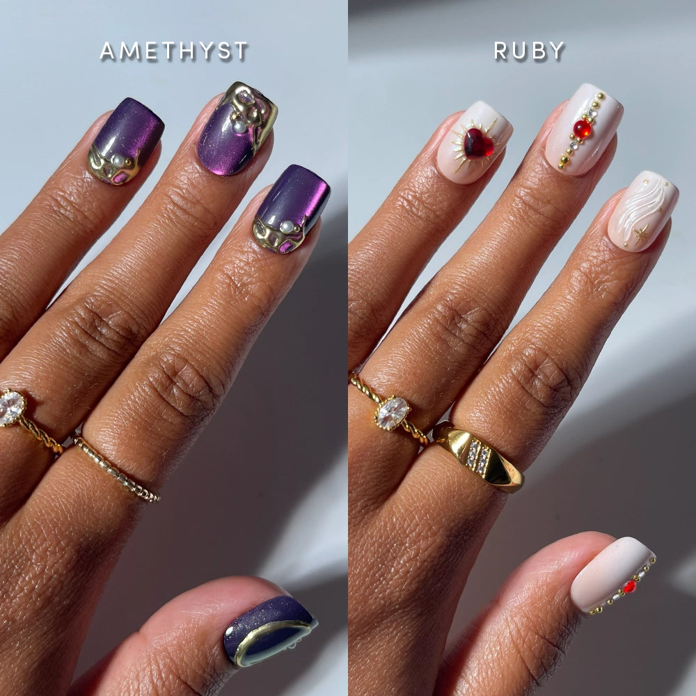 Two manicured hands with rings showcase distinct nail art: the left hand displays shimmery purple press-on nails embellished with gold and gem accents, while the right hand features glamnetic's Squoval Stones press-on nails in a short squoval shape, adorned with white polish, red gems, gold lines, and 3D heart nail art.