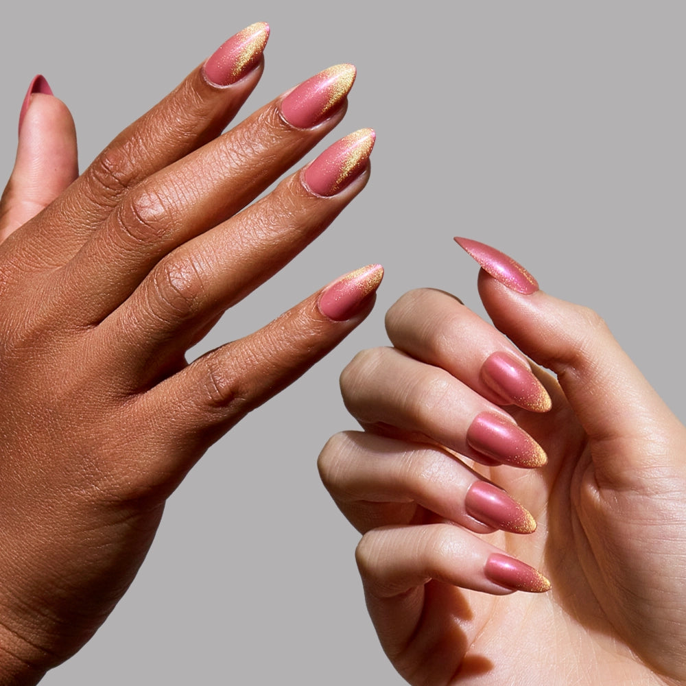 Two hands with short almond nails in glamnetic's Starbeam—a pink base with gold glitter tips—are displayed against a plain gray background, one on light skin and the other on dark skin. - Product image