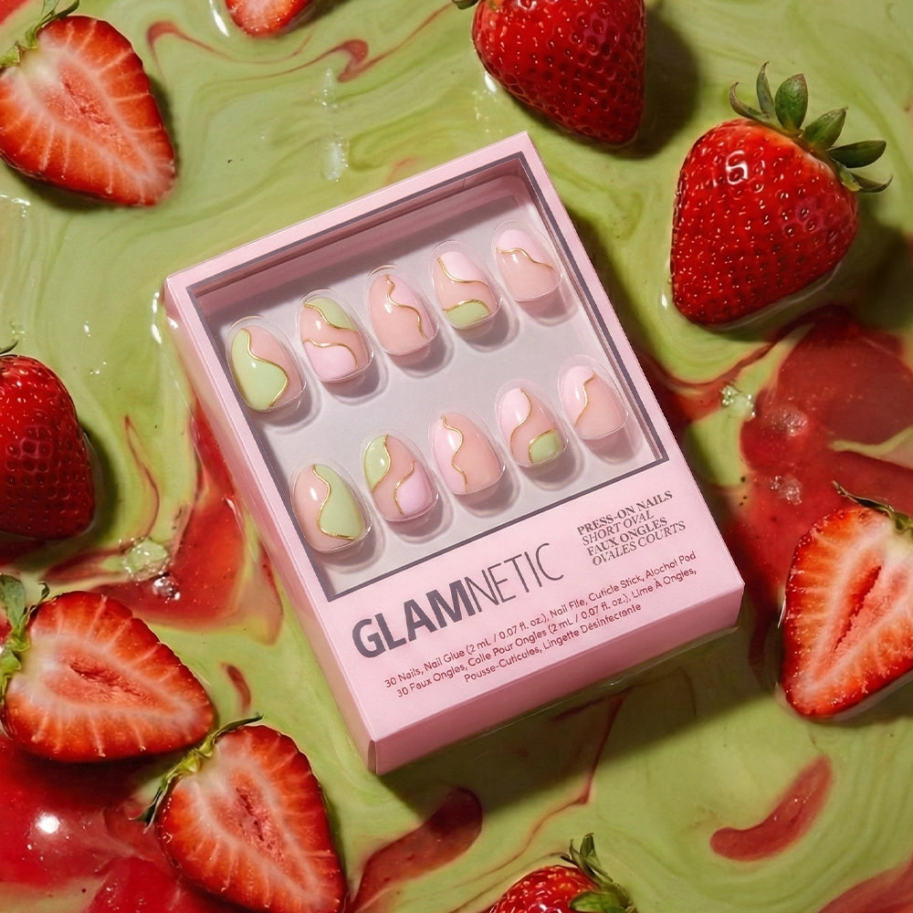 A box of glamnetic Strawberry Matcha Press-On Nails sits on a surface with strawberries and swirled red-green sauce, evoking café vibes with sliced and whole strawberries surrounding the chic set. - Product image