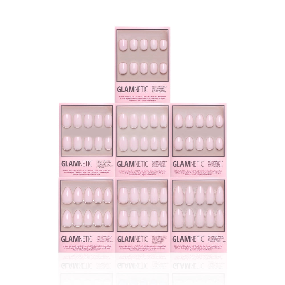 Seven boxes of the glamnetic Strawberry Milk Bundle are stacked in a pyramid on a white background, each showing semi-transparent, oval-shaped soft pink press-on nails through a clear window. - Product image