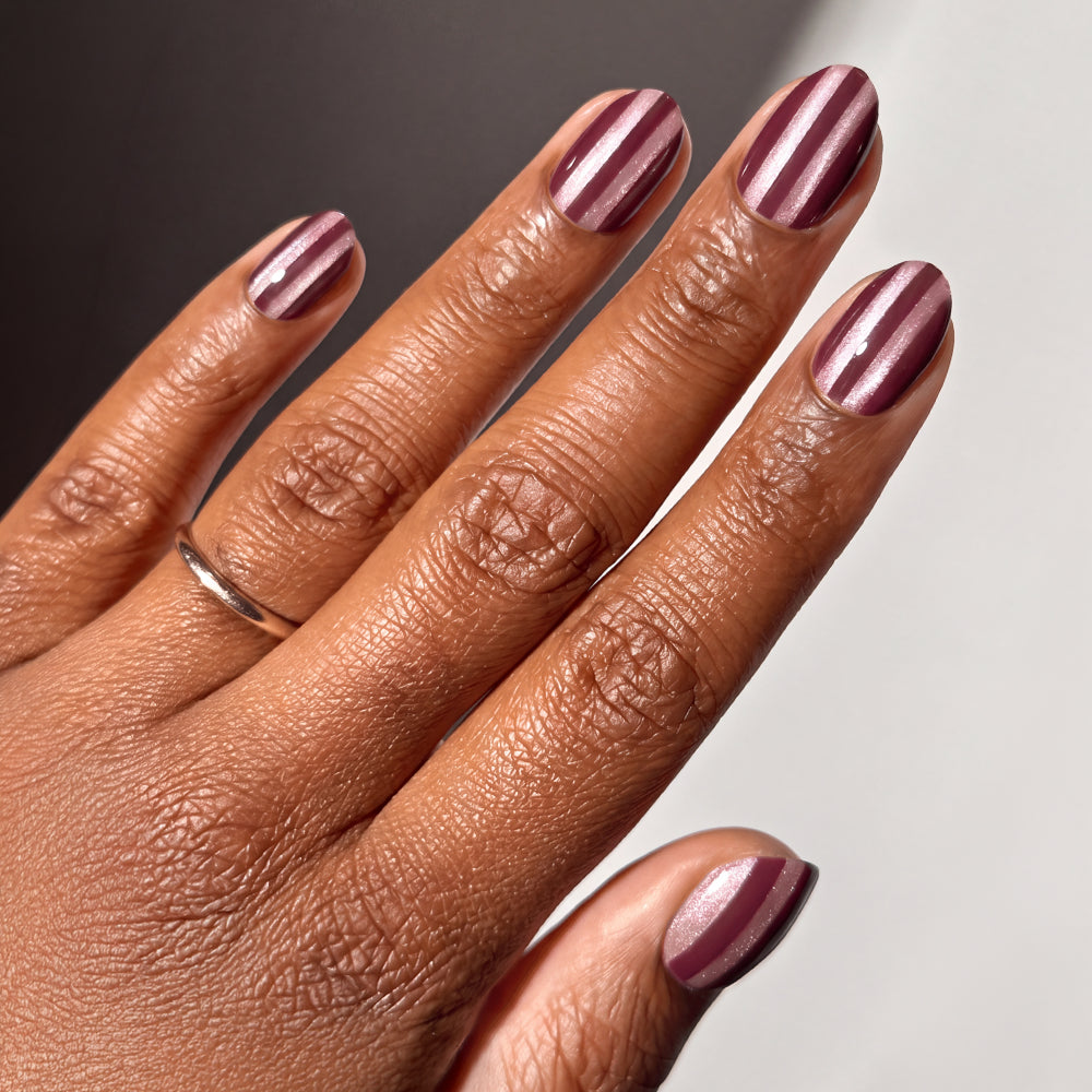 Hand with short oval almond-shaped nails featuring vertical metallic burgundy and light pink Sugar Stripes vegan nail set.