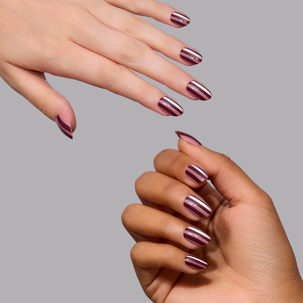 Two hands wearing Glamnetic Sugar Stripes, featuring short, almond-shaped vegan press-on nails with glossy burgundy and metallic silver vertical stripes. - Product image