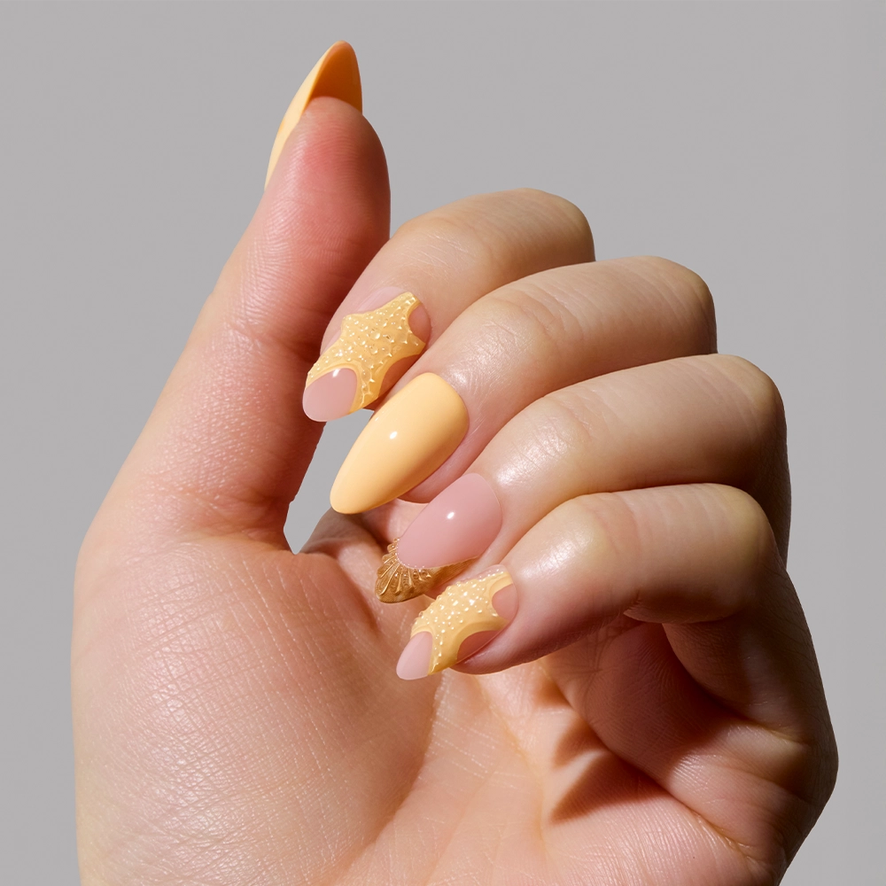 A hand with almond-shaped nails painted in pastel yellow and nude pink, featuring glamnetics Sunny Shores design with textured, wavy yellow accents on two nails, reminiscent of seashells, set against a plain gray background. - Product image