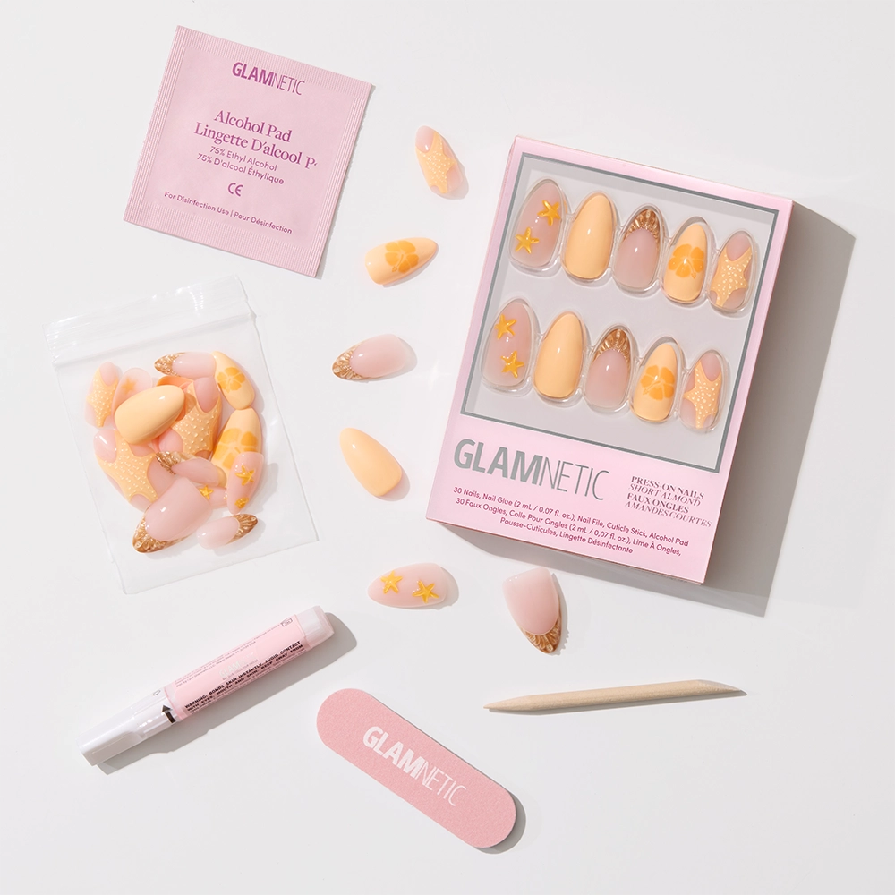 A flat lay of the glamnetic Sunny Shores Press-On Nail Set in peach and yellow star designs, shown with an alcohol pad, nail glue, file, cuticle stick, and extra nails on a white background for mermaid-inspired manicures. - Product image
