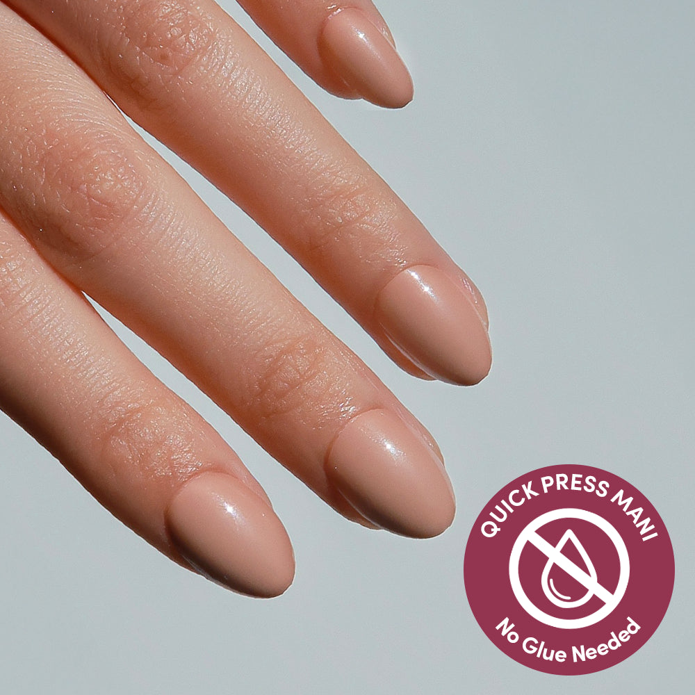 A hand with neatly manicured, nude-colored glamnetic Teddy press-on nails is shown. A circular icon reading “Quick Press Mani, No Glue Needed” highlights these no-glue nails, with a crossed-out droplet graphic in the corner.