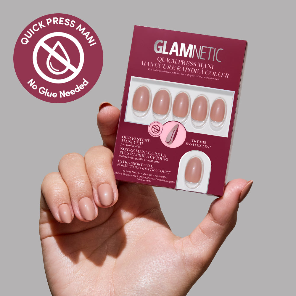 A hand with neatly manicured nails holds a pink and white box of glamnetic Quick Press Mani no-glue press-on nails in the shade "Teddy," featuring a “No Glue Needed” badge in the top left corner.