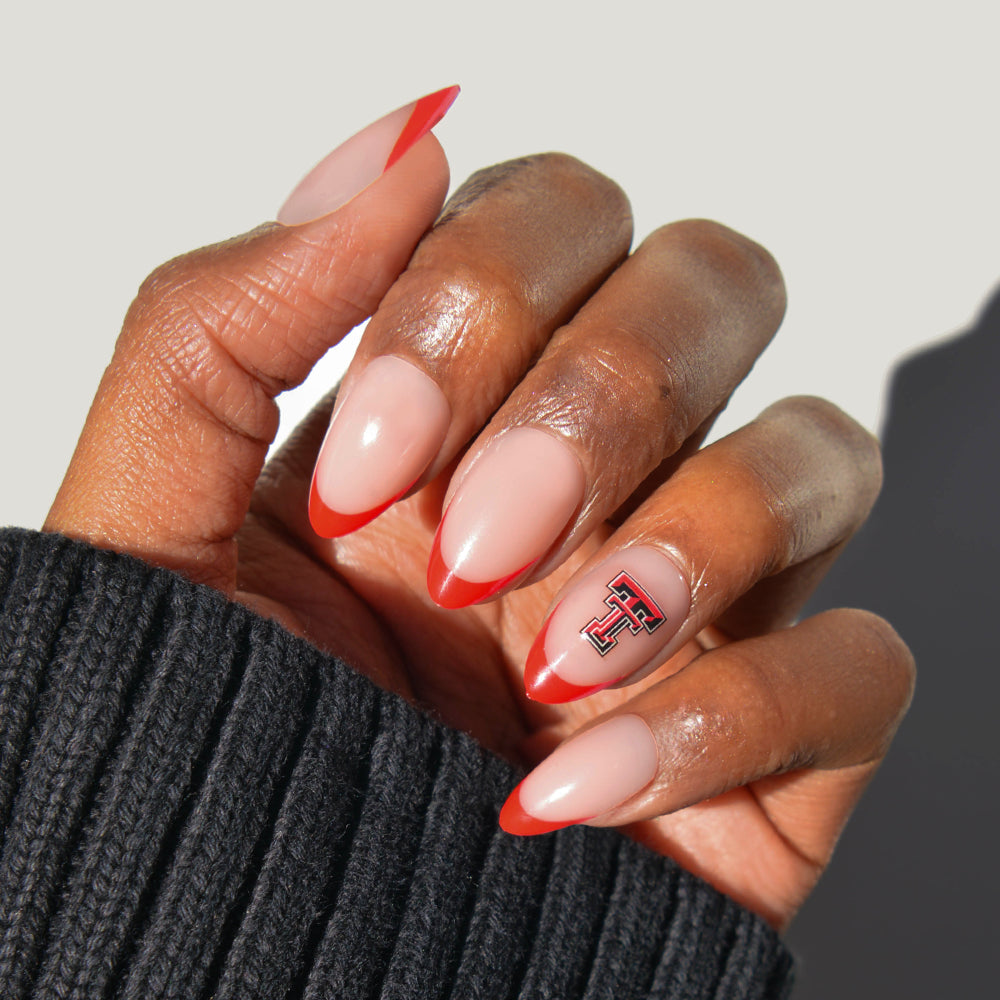 A hand with almond-shaped glamnetic Collegiate Press-On Nails, featuring red tips and an accent nail with a black and red “T” logo, paired with a ribbed black sweater. - Product image