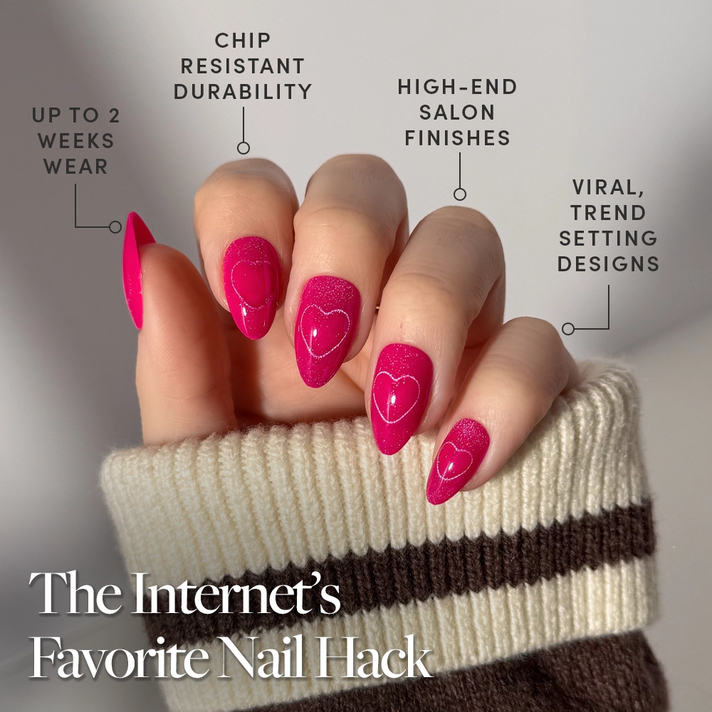 A hand with glossy, hot-pink velvet "Text Me Back" nails by glamnetic in heart patterns is shown. Features include up to 2 weeks’ wear, chip-resistant durability, salon-quality finish, and viral designs. Sweater sleeves are visible. - Product image
