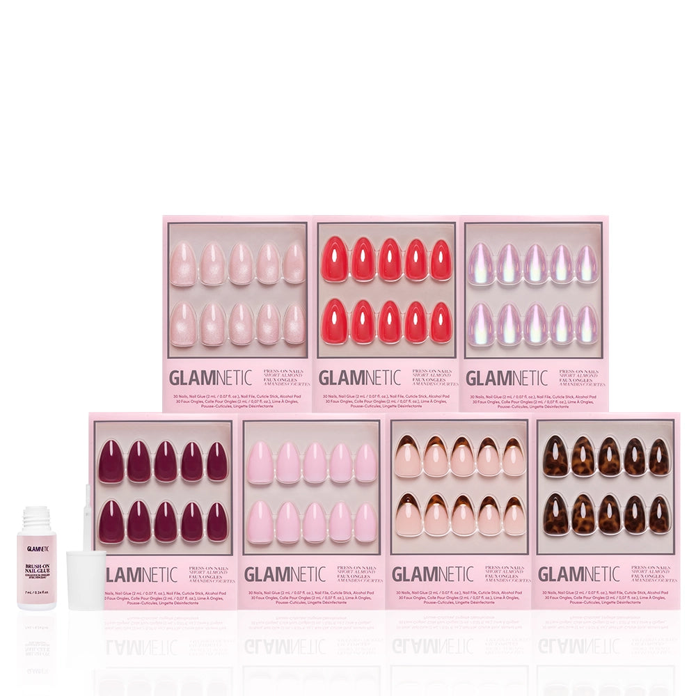 Nine sets of glamnetic’s The Short Almond Edit, in pink and neutral shades, are arranged in two rows. A small nail glue sits to the left, with all items displayed on a sleek white reflective background. - Product image