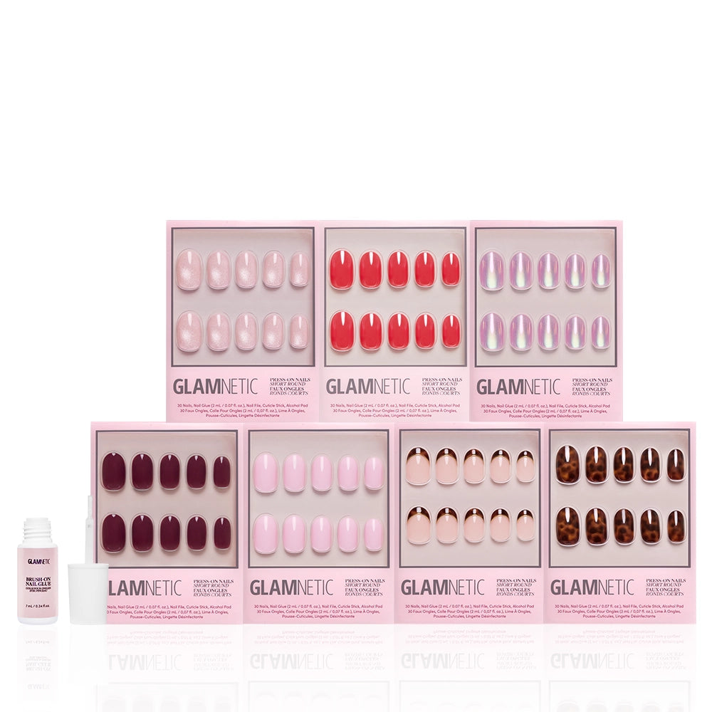Eight boxes of glamnetic's The Short Round Edit press-on nails in pink, red, and brown shades are arranged in two rows, forming a chic mani set. A nail glue bottle sits to the left on a white background. - Product image