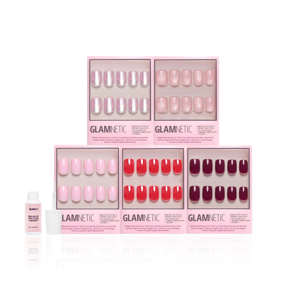 Six boxes of glamnetic’s The Short Squoval Edit press-on nails are shown in pink, red, and burgundy shades with a small bottle of nail glue on the left, all set against a crisp white background. - Product image