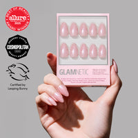 A hand with pink glazed nails holds a glamnetic Barely Spotted press-on nail box showing ten glossy pink nails. Beauty award badges and a Leaping Bunny cruelty-free certification appear on the left.